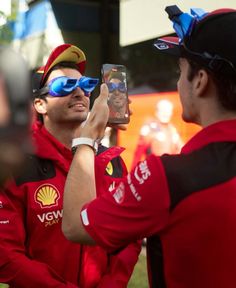 two men in red uniforms are taking pictures with their cell phones while wearing goggles