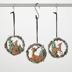 three ornaments hanging from a metal rod with deer and pine cones on them, in the shape of wreaths