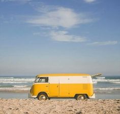 a yellow and white van parked on top of a sandy beach next to the ocean