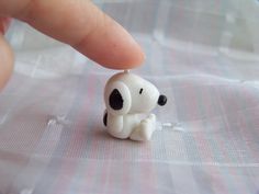 a tiny toy dog sitting on top of a white cloth covered table next to a person's finger