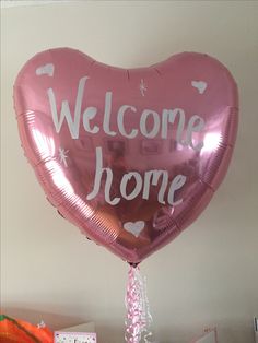 a heart shaped balloon with the words welcome home written on it, hanging from a wall