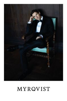 a man in a tuxedo sitting on a chair with his hand under his chin