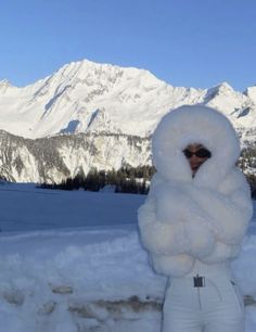 a woman standing in the snow with her arms wrapped around her shoulders and wearing white pants