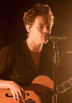 a young man playing an acoustic guitar in front of a microphone