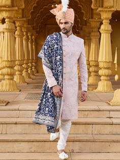 a man standing on some steps wearing a blue and white outfit with a pink turban