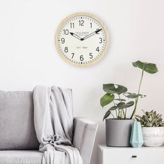 a living room with a gray couch and a clock on the wall above it, next to potted plants