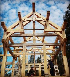 two men are working on the framing of a wooden structure with blue skies in the background