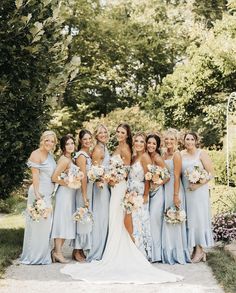 a group of women standing next to each other in front of trees and bushes with bouquets