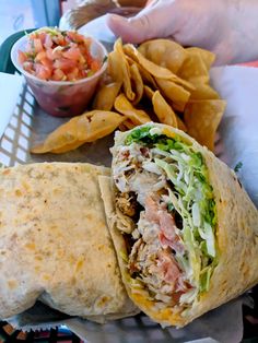 a close up of a burrito on a tray with chips and salsa in the background