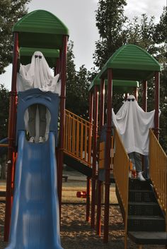 two children's play structures with plastic ghost costumes on them and one child climbing down the slide