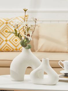 two white vases with flowers in them sitting on a table next to a couch