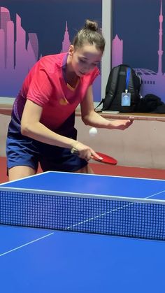 a woman in pink shirt and blue shorts playing ping pong with racket on table