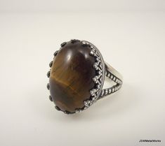 Large, bold and simply stunning. This large sterling silver tiger's eye ring is perfect for the individual who loves detail in every aspect of their lives. A large 18 x 13 mm tiger's eye cabochon is nestled in a beautiful sterling silver base, which has a victorian filigree design that adds to the beauty of the stone. The ring base is 3mm wide and 0.9mm thick, giving it a sturdy, yet very comfortable feel. This ring is available in a size 7. Tiger's eye is the gemstone associated with the 9th ye Brown Oval Gemstone Rings, Elegant Brown Rings With Natural Stones, Brown Oval Cabochon Rings, Brown Sterling Silver Cabochon Ring, Brown Sterling Silver Ring With Cabochon, Sterling Silver Rings With Brown Natural Stones, Brown Sterling Silver Rings With Natural Stones, Oval Brown Rings With Natural Stones, Brown Oval Rings With Natural Stones