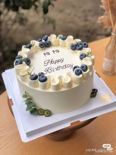 a birthday cake with white frosting and blueberries on top sits on a table