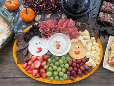 a platter filled with fruit, crackers and meats next to other snacks