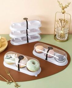 three donuts in plastic trays on a table next to a cup and saucer