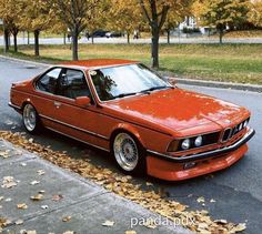 an orange bmw is parked on the side of the road in front of some trees