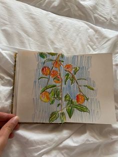 an open book with drawings of flowers and leaves in it on a white bed sheet