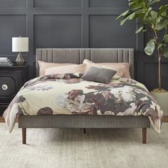 a bed with a floral comforter and pillows on top of it next to a night stand