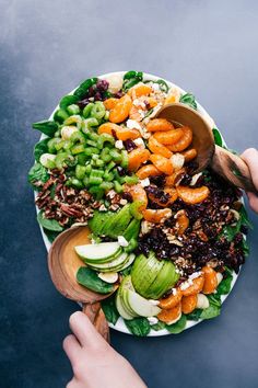 a person is holding a wooden spoon over a salad