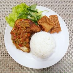 a white plate topped with meat, rice and lettuce on top of a table