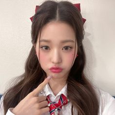 a girl with long brown hair wearing a red and white tie, holding her finger to her lips