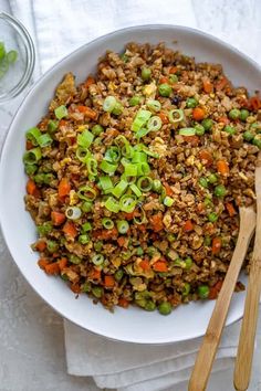 a white bowl filled with rice and veggies next to wooden utensils