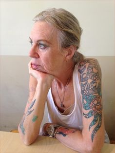 a woman sitting at a table with tattoos on her arms and shoulder, looking to the side