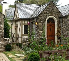 a stone house with a wooden door and bench in the front yard, surrounded by greenery