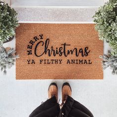 a person standing in front of a door mat that says merry christmas ya filthy animal