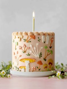 a birthday cake decorated with mushrooms and candles on a pink table next to white flowers