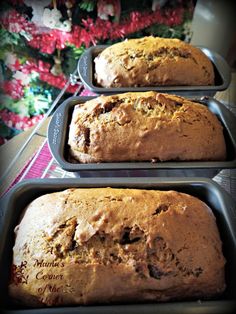 three loafs of banana bread sitting in pans on top of a table next to a christmas tree