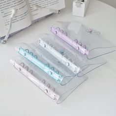 four different colored pens sitting on top of a white table next to an open book