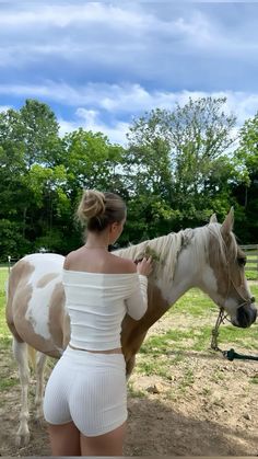 a woman standing next to a brown and white horse