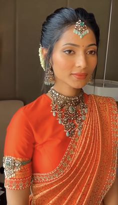 a woman in an orange sari with jewelry on her neck and headpieces