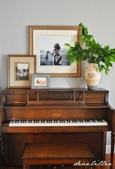 there is a piano in the room with pictures on the wall and a potted plant next to it