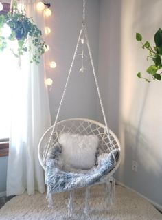 a hanging chair in the corner of a room with white rugs and pillows on it