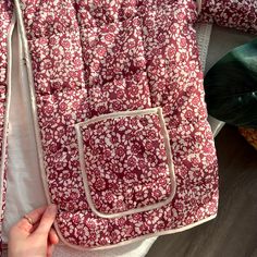 a person is holding onto a red and white floral quilted bag with zippers