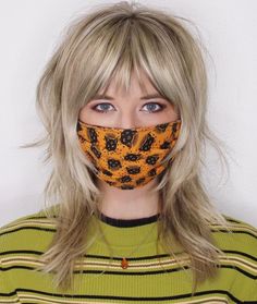 a woman with blonde hair wearing a leopard print face covering over her mouth and looking at the camera