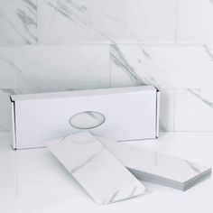 a white box with four sheets of paper in front of it on a marble countertop