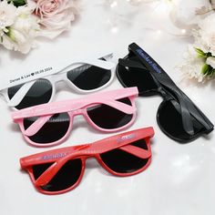 three pairs of sunglasses sitting on top of a white table next to pink and black flowers