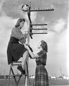 two women sitting on top of a sign post