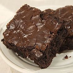 two chocolate brownies on a plate with one cut in half and the other partially eaten