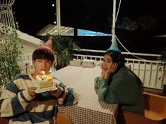 two people sitting at a table with a cake in front of them and one holding a candle