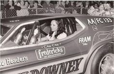 an old photo of a woman in a race car with fans watching from the stands