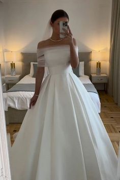 a woman in a white wedding dress taking a selfie with her cell phone while standing next to a bed