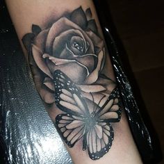 a black and white rose with a butterfly tattoo on the arm that is sitting on a table