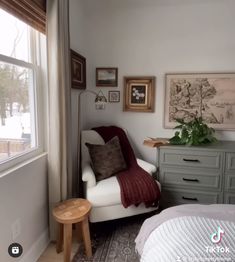 a bedroom with a white chair and some pictures on the wall next to a window