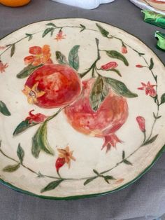 a plate with fruit painted on it sitting on a table next to other plates and utensils