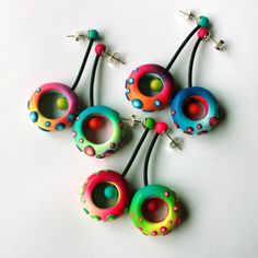 five colorful beads are arranged on a white surface with ear wires attached to the ends